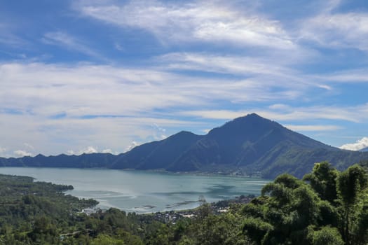 Mountain lake in the volcanic caldera of Batur under Mount Abang on the island of Bali, Indonesia. Quiet level of a large drinking water reservoir. High mountain peaks rise above the lake. Blue sky.