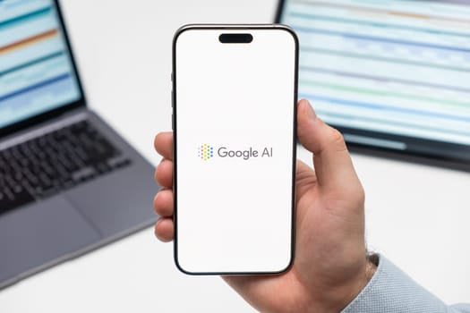PRAGUE, CZECHIA - JULY, 2024: Google Ai logo on the screen of smartphone in mans hand and laptop on the background