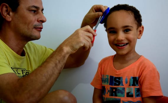 salvador, bahia / brazil - july 7, 2020: father cuts his son's head at home during social isolation due to the pandamine of the corona virus in the city of Salvador.