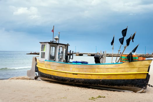 Old and rusty fishing boat and equipment on sandy beach, getting ready for fishing trip. Pier and blue sea in background, Niechorze, Poland