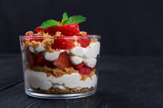 Strawberry with cookie and cream dessert decorated with mint leaf on black wooden background