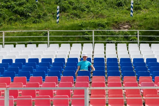 Lonely boy on the empty stadium outdoor. Empty tribune due to pandemic Covid-19. Concept of pandemic life , empty stadiums, distance from viewers, safety.