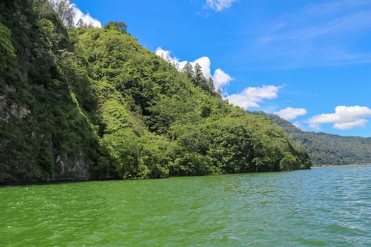 Sailing a traditional fishing boat from the village of Trunyan to a unique cemetery. High mountains covered with dense tropical vegetation line the coast of Lake Batur on the island of Bali, Indonesia