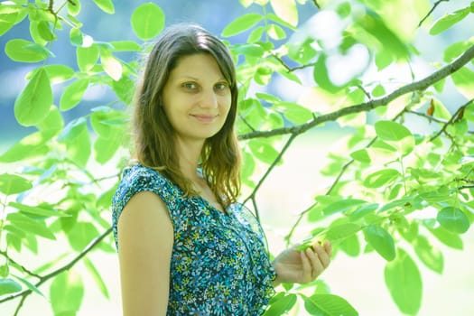 Girl smiles against a branch with green leaves in sunny weather