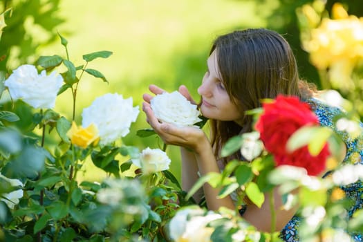 Young girl enjoys the scent of roses in the park