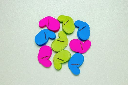 Colourful set of nine plastic clothespins or pegs on a light green sparkling background with copy field. View from above.
