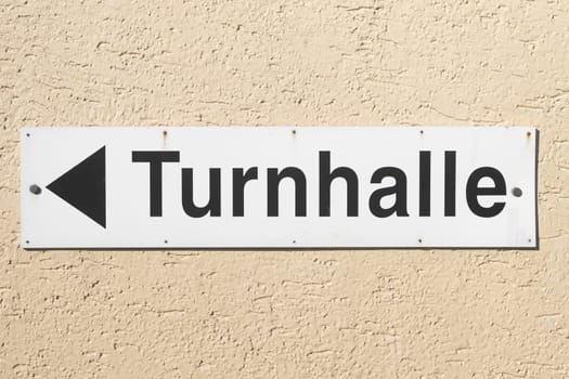 Gym Sign in german language hanging on house fassade with black arrow