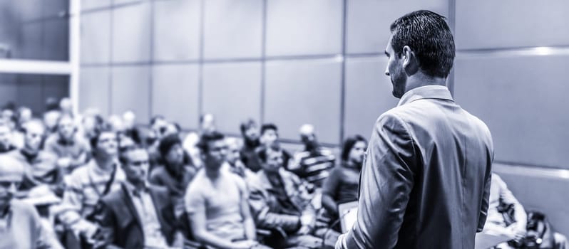 Speaker giving a talk on corporate business conference. Unrecognizable people in audience at conference hall. Business and Entrepreneurship event.