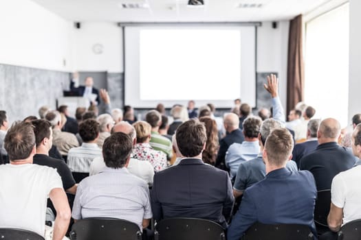 I have a question. Group of business people sitting at the chairs in conference hall. Businessman raising his arm. Conference and Presentation. Business and Entrepreneurship.