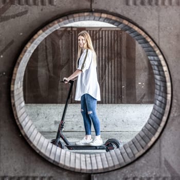 Casual caucasian teenager riding urban electric scooter in urban environment. Urban mobility concept.