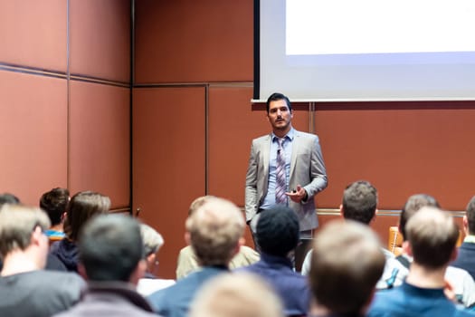 Speaker giving a talk in conference hall at business meeting event. Rear view of unrecognizable people in audience at the conference hall. Business and entrepreneurship concept.