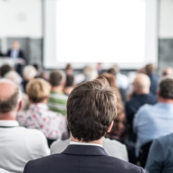 Speaker giving a talk in conference hall at business event. Audience at the conference hall. Business and Entrepreneurship concept. Focus on unrecognizable people in audience.