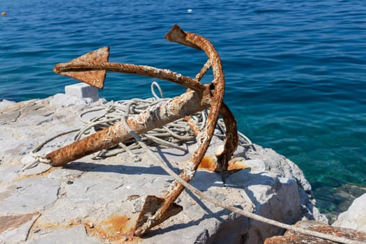 Old rusty anchor on rock by blue adriatic sea.