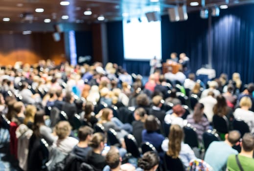 Business and entrepreneurship symposium. Speaker giving a talk at business meeting. Audience in conference hall. Rear view of unrecognized participant in audience.