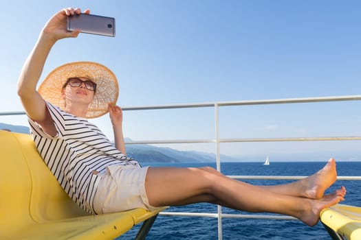 Beautiful, romantic blonde woman taking selfie self portrait on summer vacations traveling by cruse ship ferry boat. Summer vacation lifestyle.