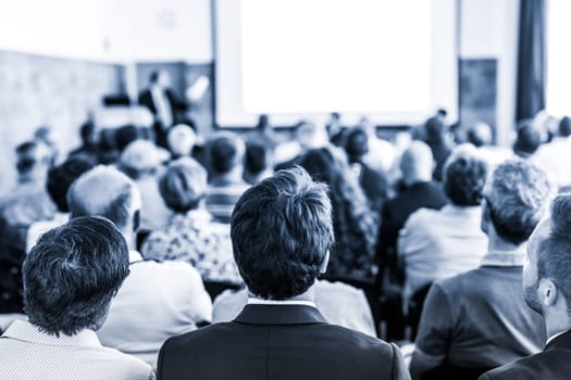 Speaker giving a talk in conference hall at business event. Audience at the conference hall. Business and Entrepreneurship concept. Focus on unrecognizable people in audience. Blue toned.