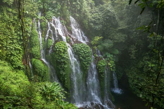 Beautiful scenic waterfall high in the mountains on Bali island. Water flows in many streams over the glass and between them grows lush tropical vegetation. Banyumala Amertha Waterfall, Indonesia.