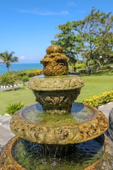 Peaceful scenery with fountain. Park near the Hindu Temple Tanah Lot, Bali, Indonesia. Small decorative fountain in tropical garden for landscape design. Stone three-stage fountain with running water.