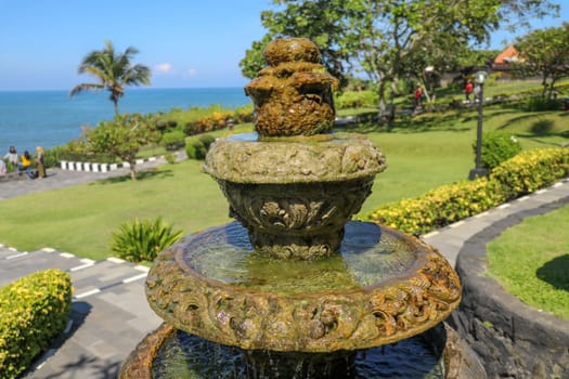 Peaceful scenery with fountain. Park near the Hindu Temple Tanah Lot, Bali, Indonesia. Small decorative fountain in tropical garden for landscape design. Stone three-stage fountain with running water.