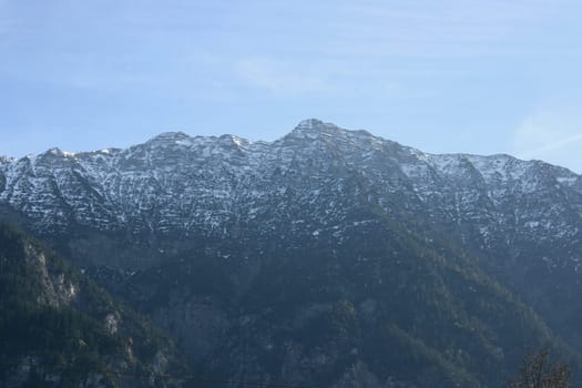 Alpine summits covered with snow, blue sky in the background .
