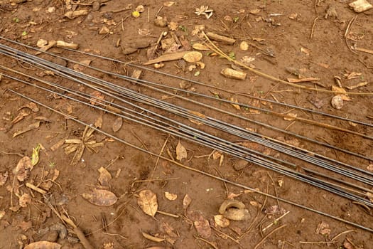 Steel rebar for reinforcement concrete at construction site with house under construction background. Steel wires laid on clay ground with dry leaves. Straight wires ready for construction.