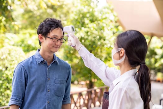 Asian waitress with face mask take temperature customer before getting in restaurant. Restaurant New normal restaurant lifestyle concept after coronavirus covid-19 pandemic.