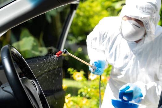 Close up of chemical alcohol spray cleaning inside car to disinfect and decontaminate coronavirus covid-19 by specialist cleaner wearing personal protective equipment PPE. New normal Hygiene concept.