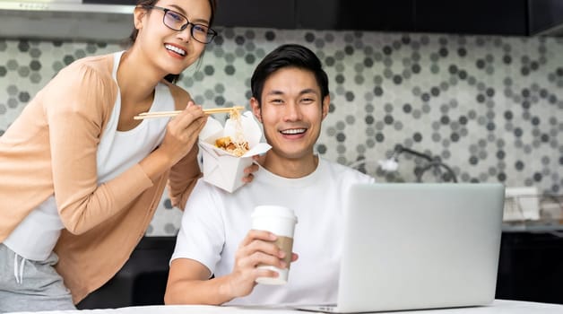 Panoramic asian couple work from home in kitchen and eat delivery chinese take away food and take out coffee while city lockdown from covid-19 pandemic. New Normal lifestyle working from home.