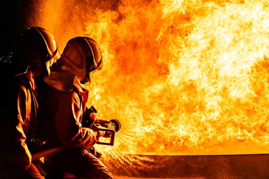 Firefighters using Twirl water fog type fire extinguisher to fighting with the fire flame from oil to control fire not to spreading out. Firefighter and industrial safety concept.