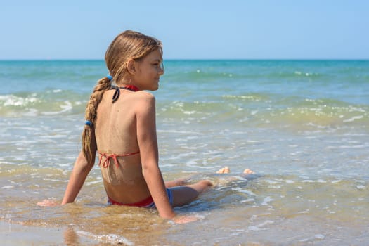 A girl of ten years old sits in the water on the sea coast