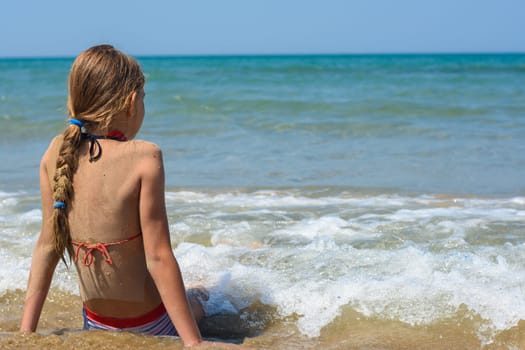 A girl sits on a sandy sea beach and looks into the distance