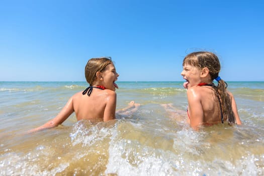 Children sit together in shallow water and show each other tongue