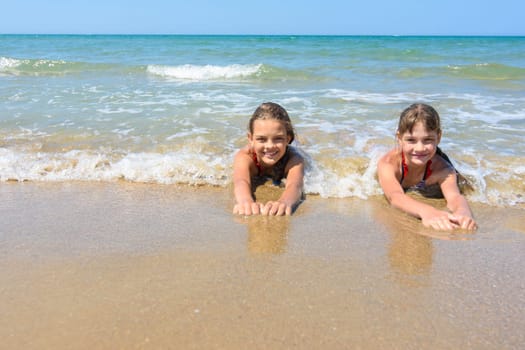 Girls lie on the sand of the sea coast and happily look at the frame