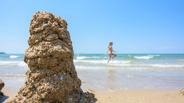 A pile of wet sand on the seashore, on the right there is an empty place for inscription, in the background a girl runs