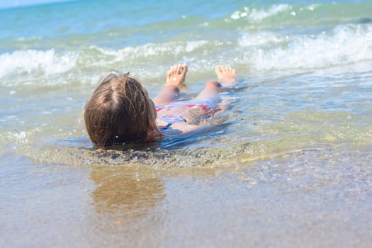 A girl lies on her back in shallow water on the sea sandy coast