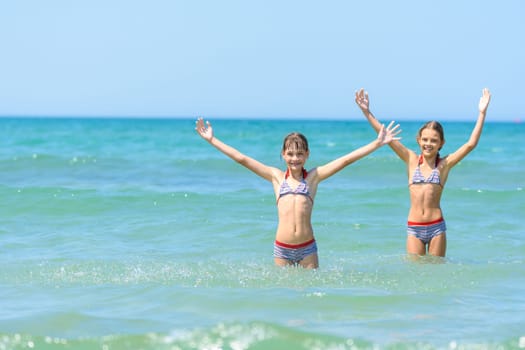 Children stand in sea water and joyfully raise their hands up