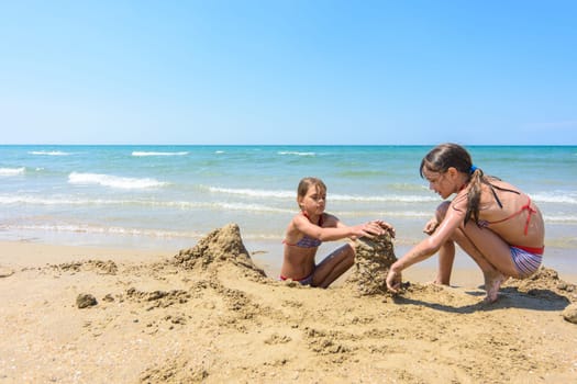Two girls play in the sand on the beach of the sea coast