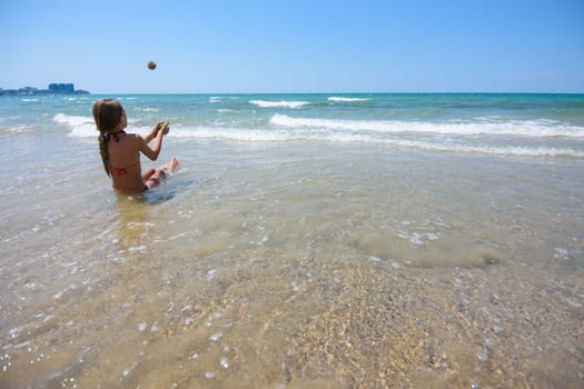 Girl sitting on the seashore and throws sand balls