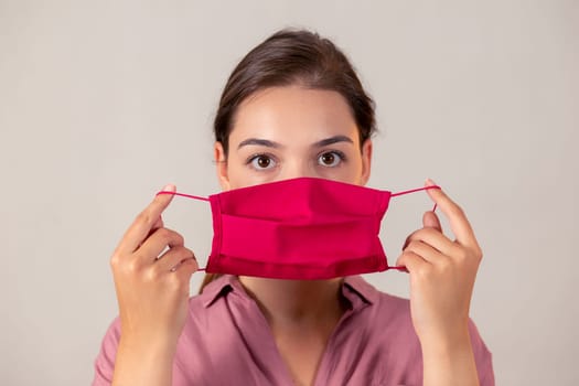 Young girl looking at the camera and preparing to put on a mask. Woman on a light background putting on a medical antiviral protection.