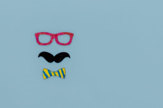 Concept image with glasses, moustache and bow tie on light blue background as resource for creative projects, copy space on the right