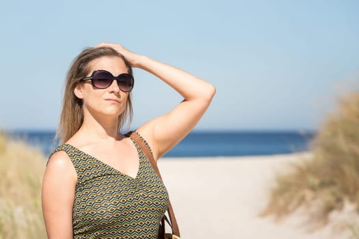 Close-up of a middle-aged blonde woman in sunglasses posing with the sea and beach on her back