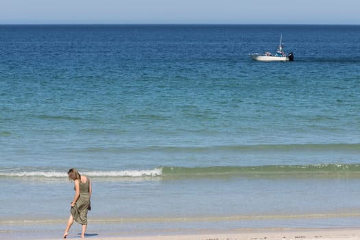 Middle-aged blonde woman in a green dress relaxes on the beach with a boat in the background