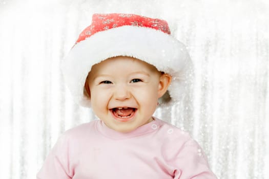 Cute baby girl with Santa hat laughing in front of silver background