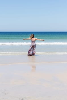 Middle-aged blonde woman relaxing at the beach with arms open enjoying her freedom facing the sea
