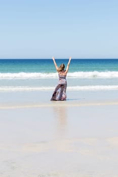 Middle-aged blonde woman relaxing at the beach with arms open enjoying her freedom facing the sea