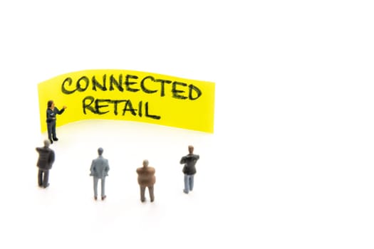 Meeting with miniature figurines posed as business people standing around post-it note with Connected Retail handwritten message in background, minimalist abstract concept with focus on text