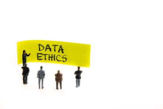 Meeting with miniature figurines posed as business people standing around post-it note with Data Ethics handwritten message in background, minimalist abstract concept with focus on text