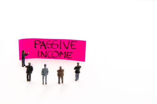 Meeting with miniature figurines posed as business people standing around post-it note with Passive Income handwritten message in background, minimalist abstract concept with focus on text