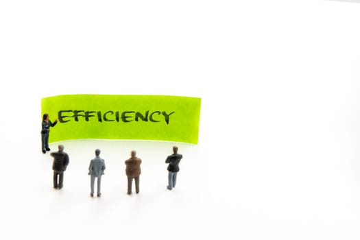 Meeting with miniature figurines posed as business people standing around post-it note with Efficiency handwritten message in background, minimalist abstract concept with focus on text