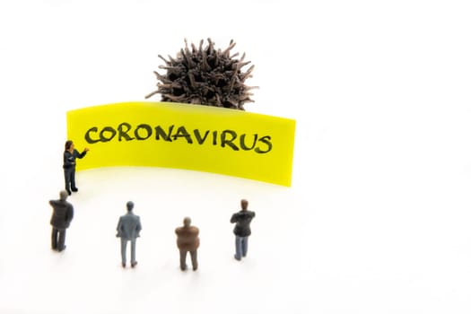 Meeting with miniature figurines posed as business people standing around post-it note with Coronavirus handwritten message in background, minimalist abstract concept with focus on text